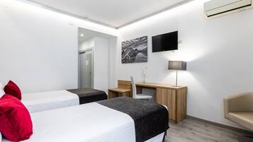 Habitación de hotel moderna con dos camas, un escritorio, una silla, un televisor y aire acondicionado instalado en la pared.