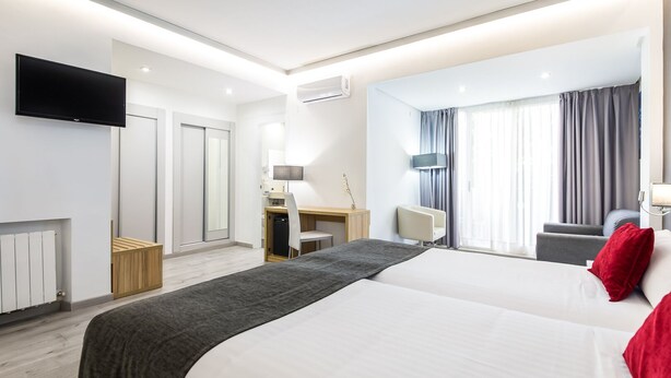 A modern hotel room with a large bed, a desk with a chair, a TV mounted on the wall, and a window with curtains. - Sweet Hotel Renasa (Valencia)