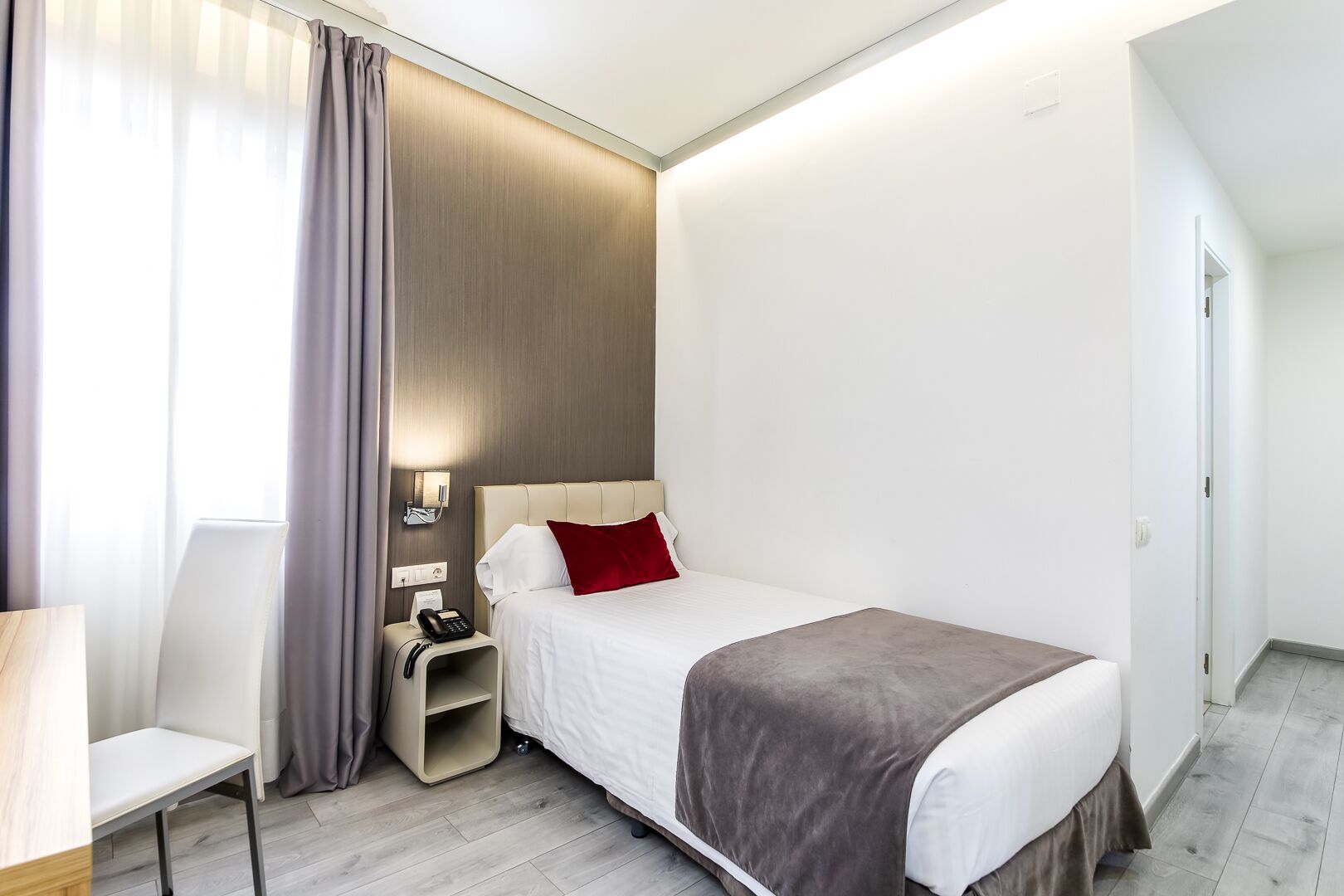 Habitació d'hotel moderna amb llit, taula de nit, cadira i escriptori petit.
