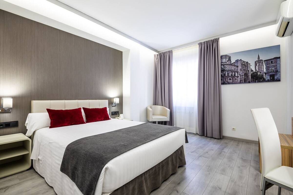 A modern hotel room with a large bed, a desk, and a chair.