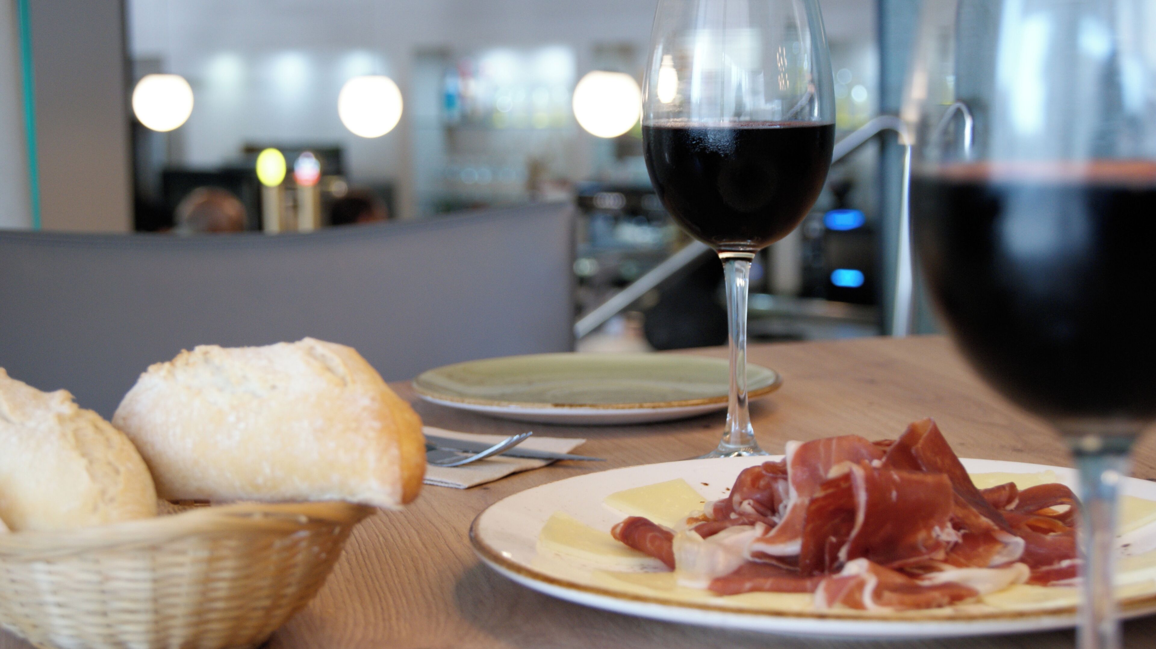 Una mesa de comedor con un plato de comida, una copa de vino tinto y una cesta de pan.