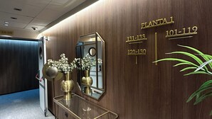A modern reception area with a wooden wall, a glass console table with brass accents, and a white leather chair. - Sweet Hotel Renasa (Valencia)