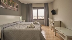 Une chambre d’hôtel avec deux lits, un bureau, une chaise, une télévision et une grande fenêtre avec des rideaux.