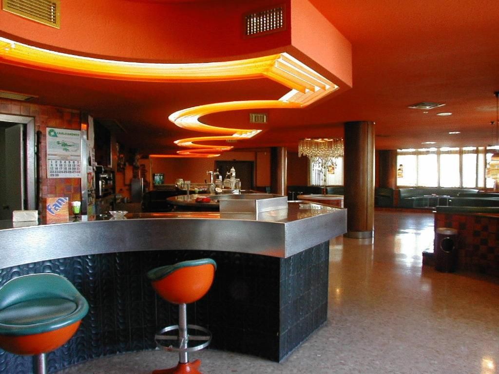 A bar area with a curved counter, two stools, and a chandelier.