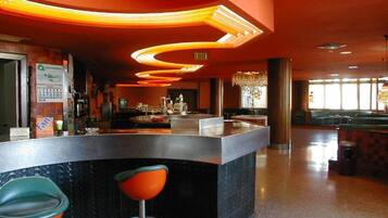A bar area with a curved counter, two stools, and a chandelier.