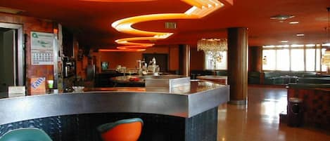 A bar area with a curved counter, two stools, and a chandelier.
