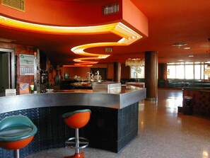 Una zona de bar con una barra curva, dos taburetes y una lámpara de araña.