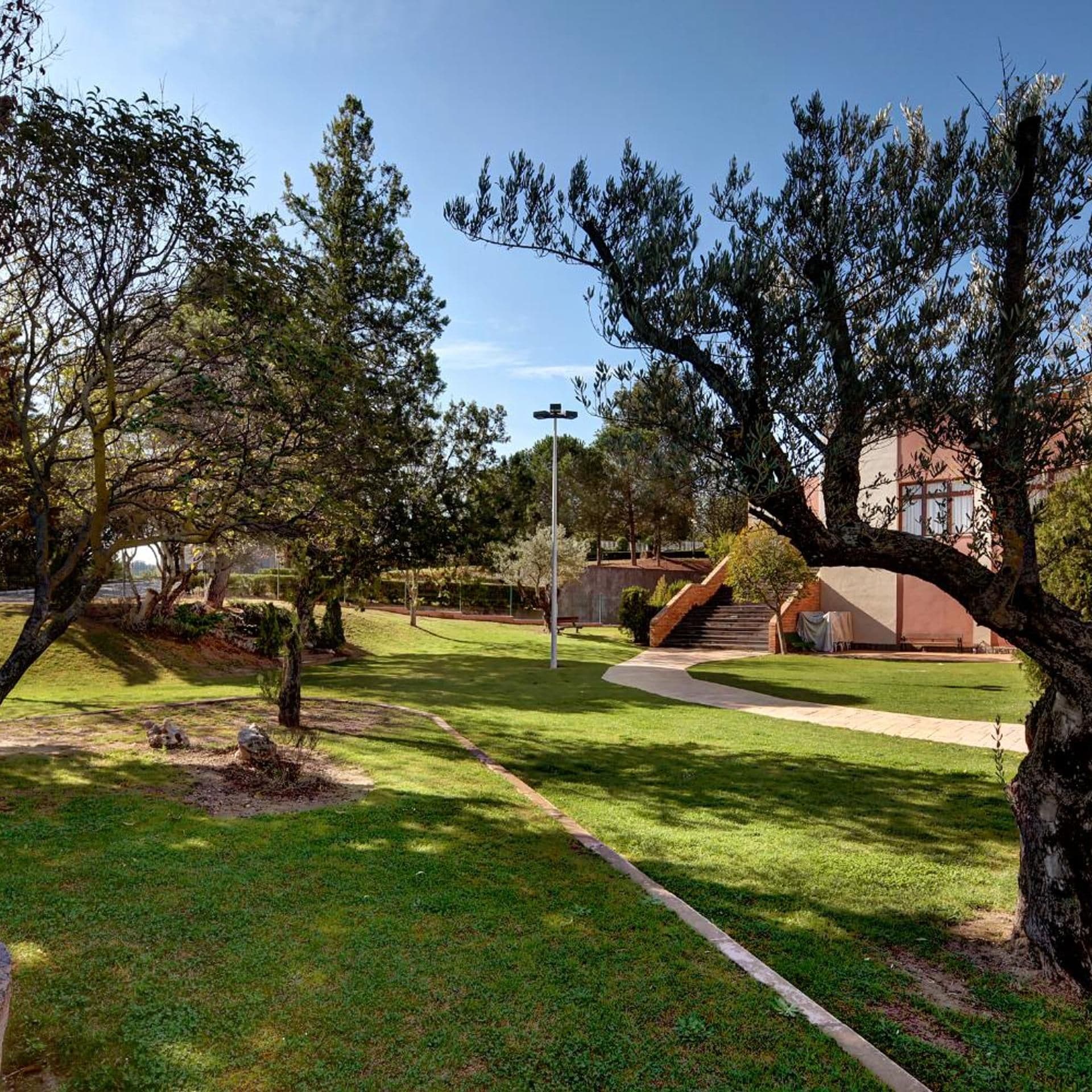Un parque con un sendero pavimentado, árboles y un edificio de fachada roja al fondo.