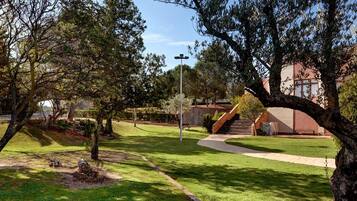 Un parque con un sendero pavimentado, árboles y un edificio de fachada roja al fondo.
