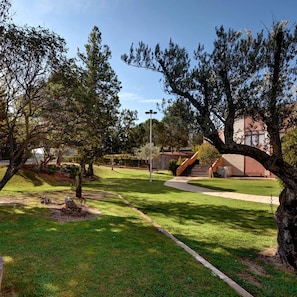 A park with a paved walkway, trees, and a building with a red facade in the background.