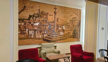 Una habitación con un gran mural que representa una escena urbana, una pequeña mesa y dos sillas rojas.