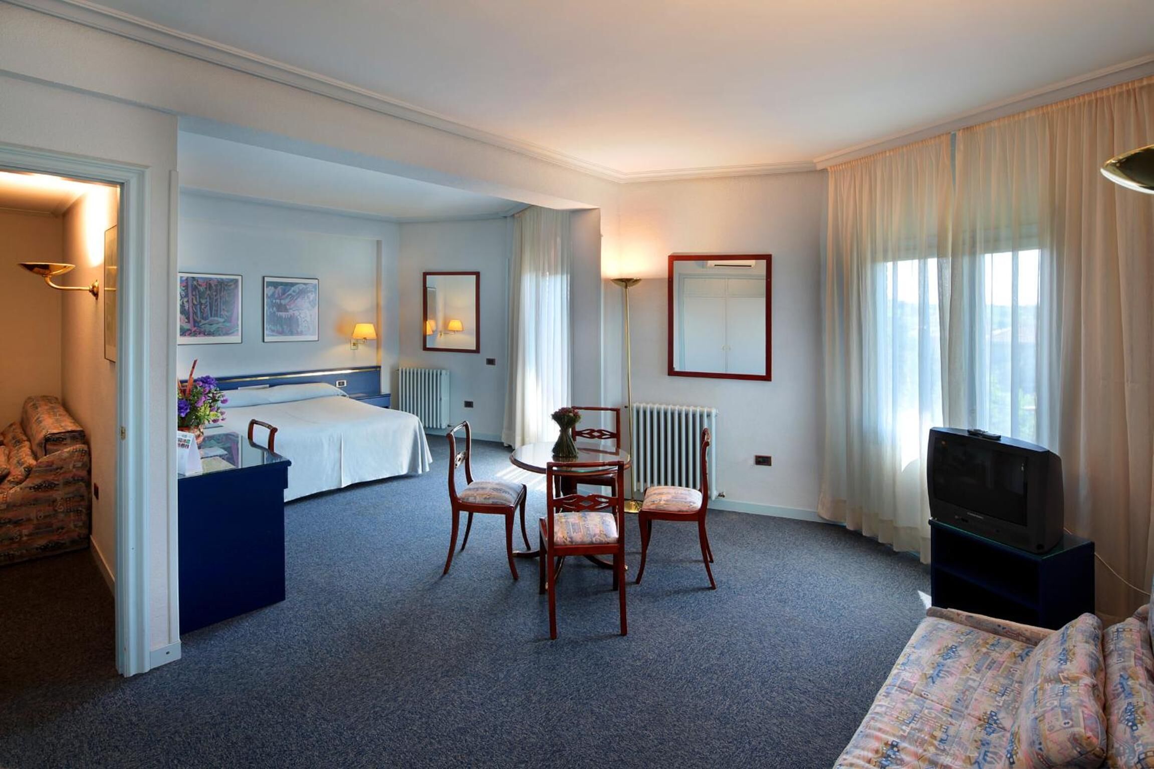 Una habitación de hotel con cama, escritorio y silla, televisor y sofá.