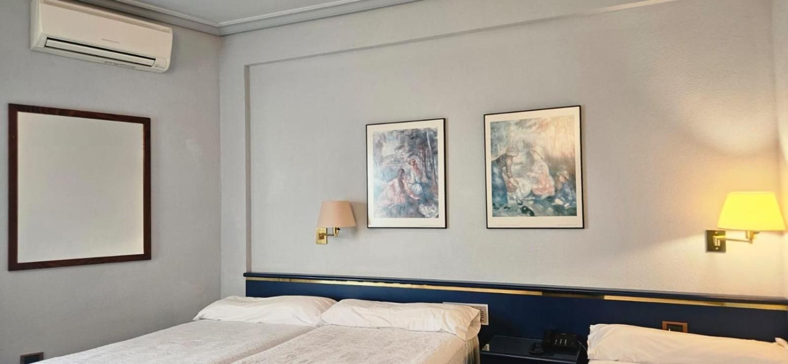 Una habitación de hotel con una cama, dos lámparas de pared y dos cuadros enmarcados.