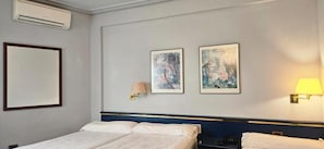 A hotel room with a bed, two wall-mounted lamps, and two framed artworks.