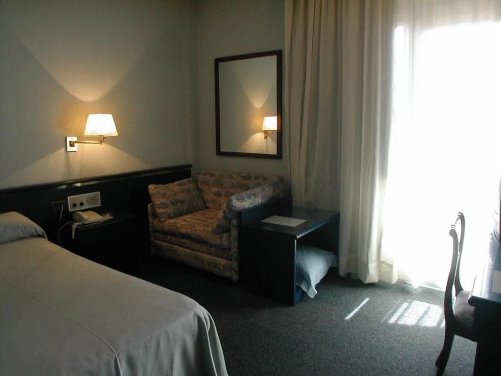 Una habitación de hotel con cama, una silla, un escritorio, una lámpara y un espejo.