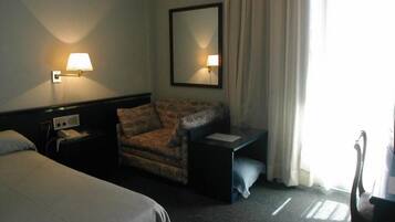 Una habitación de hotel con cama, una silla, un escritorio, una lámpara y un espejo.
