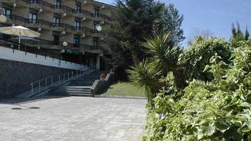 A building with multiple balconies, a paved pathway, and lush greenery.