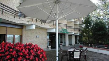 An outdoor seating area with a large umbrella, brick walls, and a building entrance.