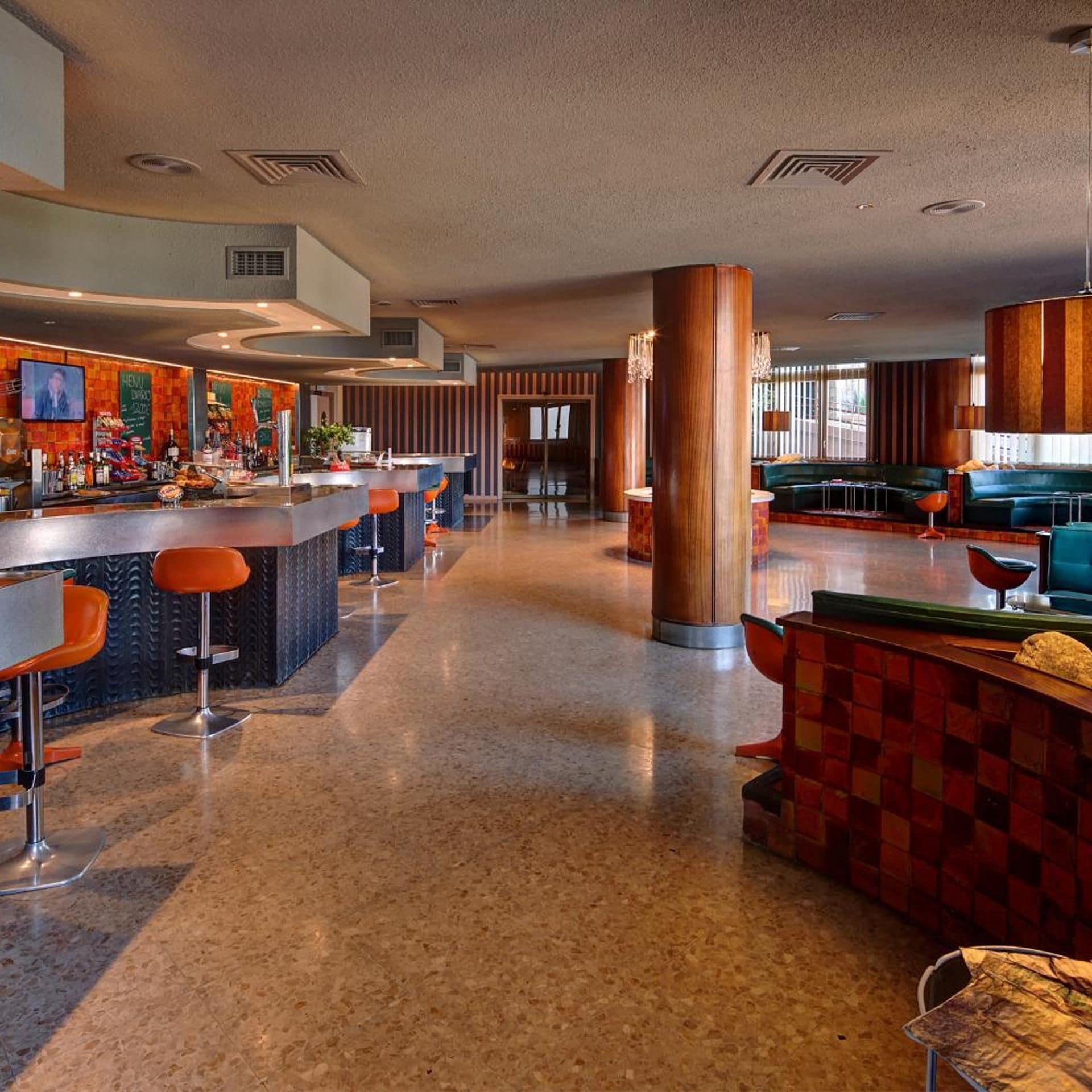 Un área de bar moderna con una barra larga, varios taburetes y un rincón de estar con sofá y sillones.