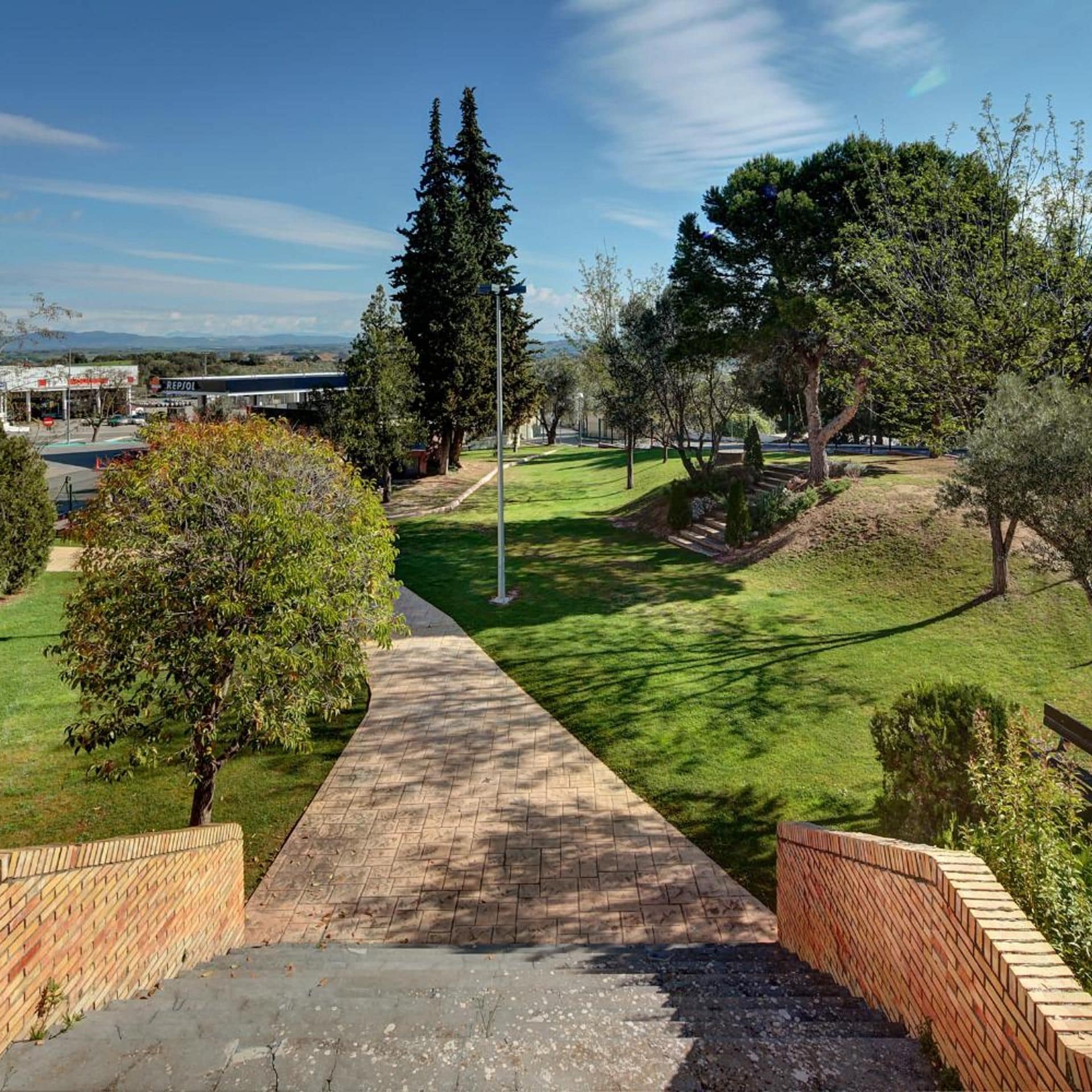 Un sendero pavimentado que atraviesa un área ajardinada con árboles y un cielo despejado.