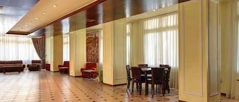 A spacious lobby with a checkered floor, seating area with sofas and chairs, and a dining table with chairs.