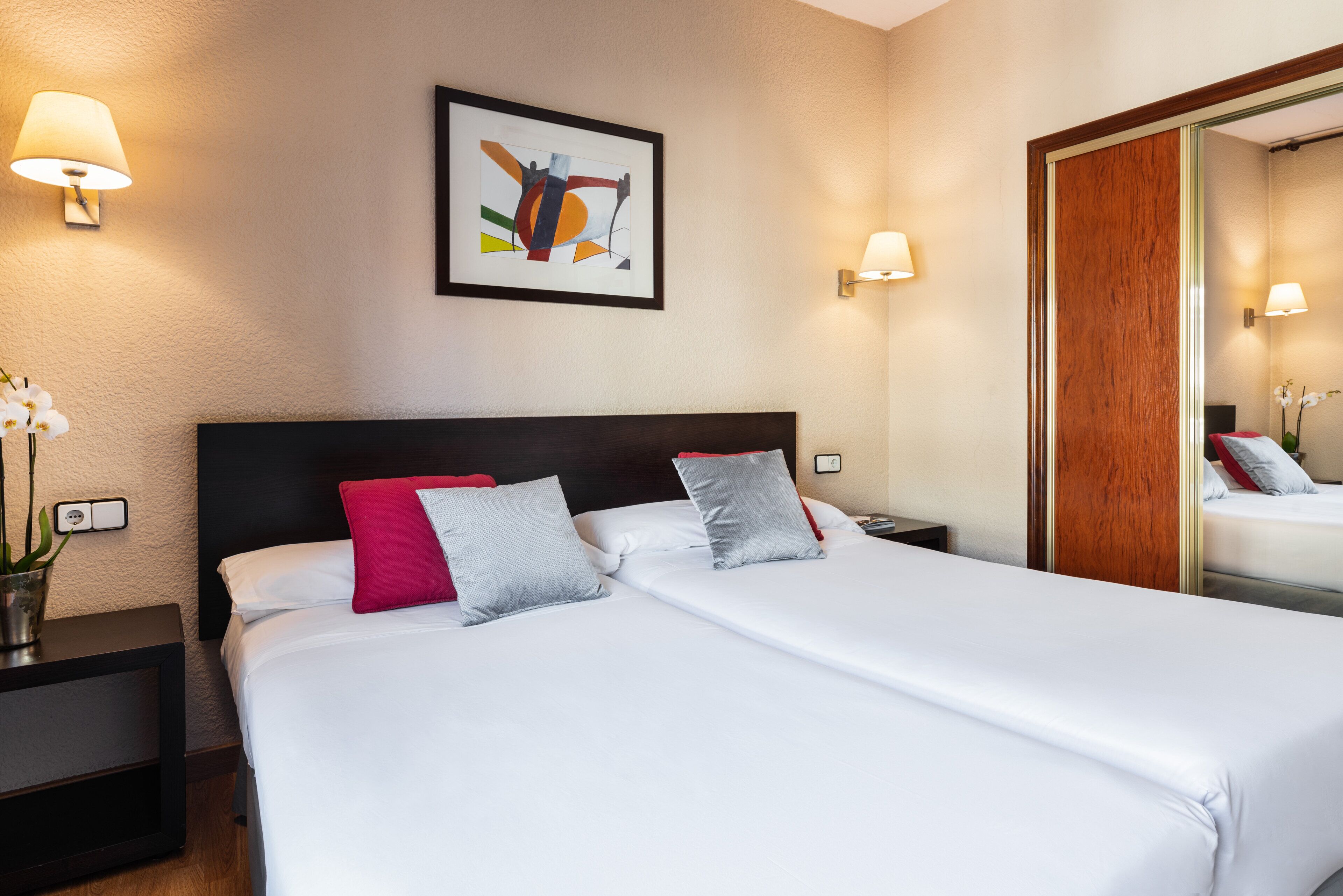 A hotel room with a large bed, two bedside tables, a nightstand, a mirror, and a framed artwork on the wall.