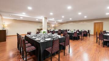 Un salón de conferencias con varias mesas dispuestas para comer, equipado con sillas y vajilla.