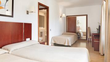 A hotel room with two beds, a desk, a chair, a mirror, and a bathroom visible through an open door.
