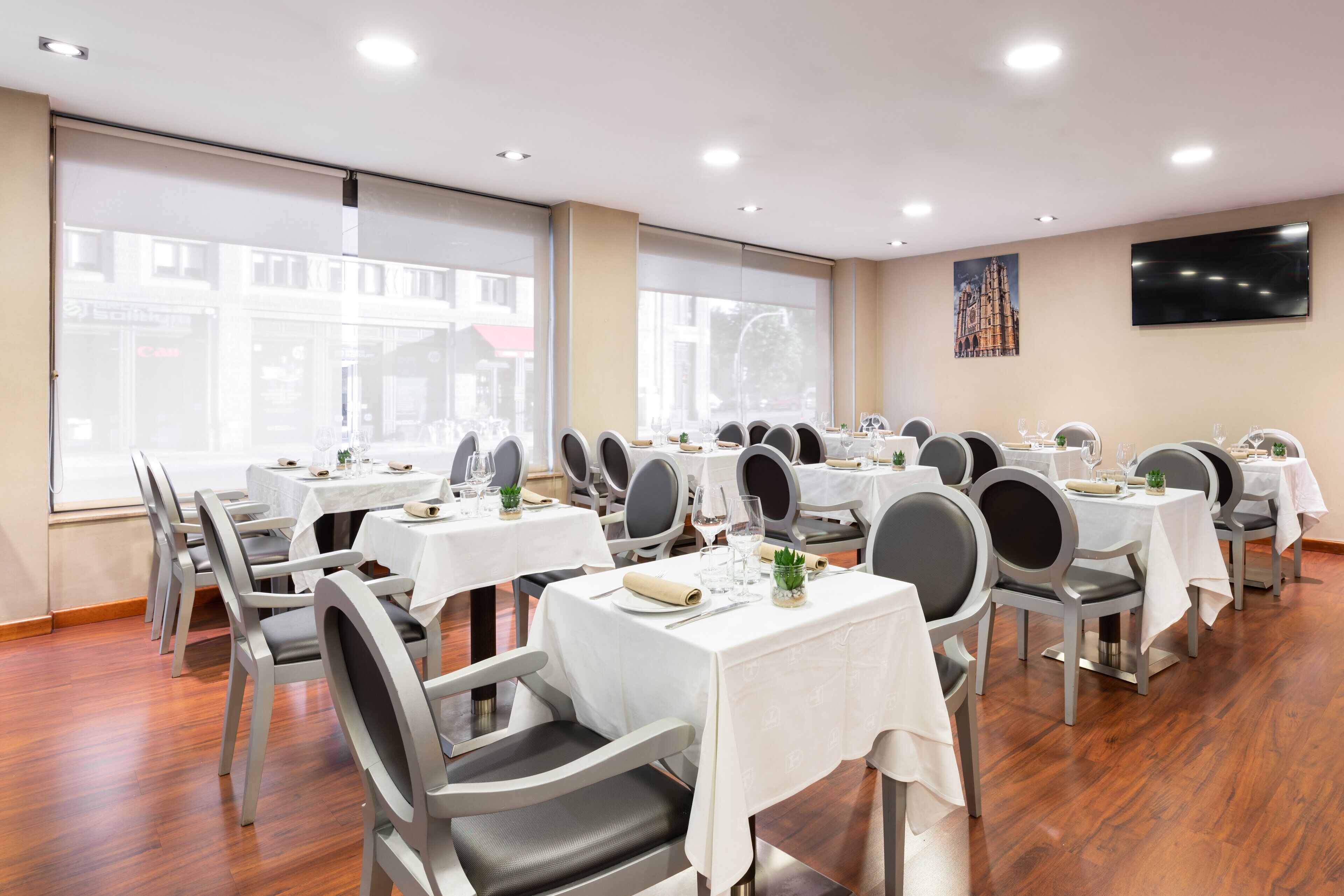 Uma sala de jantar com várias mesas e cadeiras, grandes janelas e uma televisão de tela plana na parede.