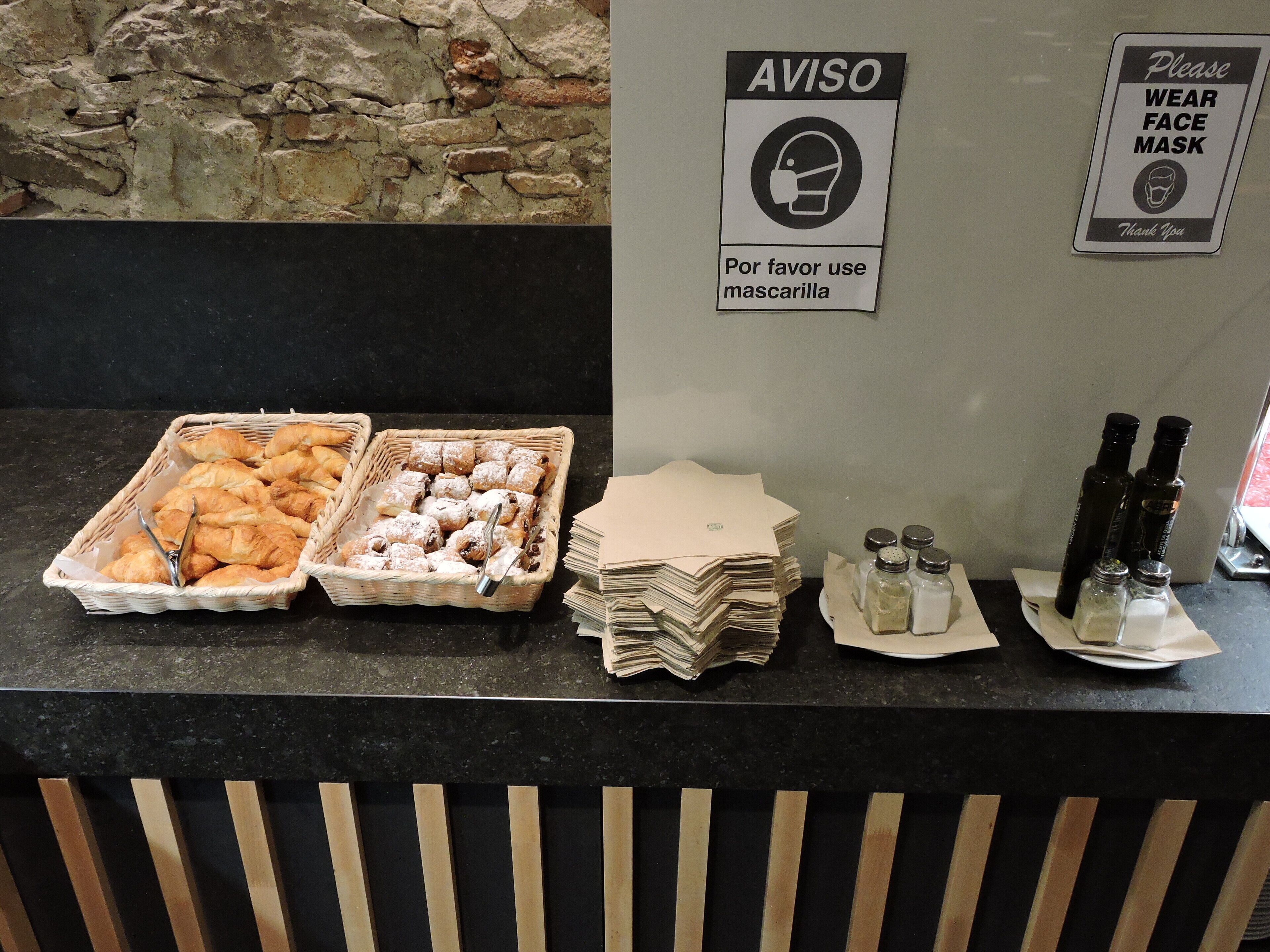 A buffet counter with pastries, condiments, and a sign requesting face masks.