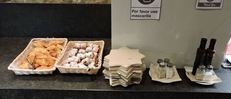 A buffet counter with pastries, condiments, and a sign requesting face masks.