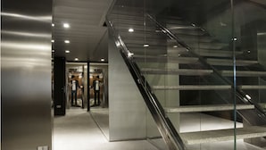 Un interior modern amb una escala de vidre i un ascensor metàl·lic.