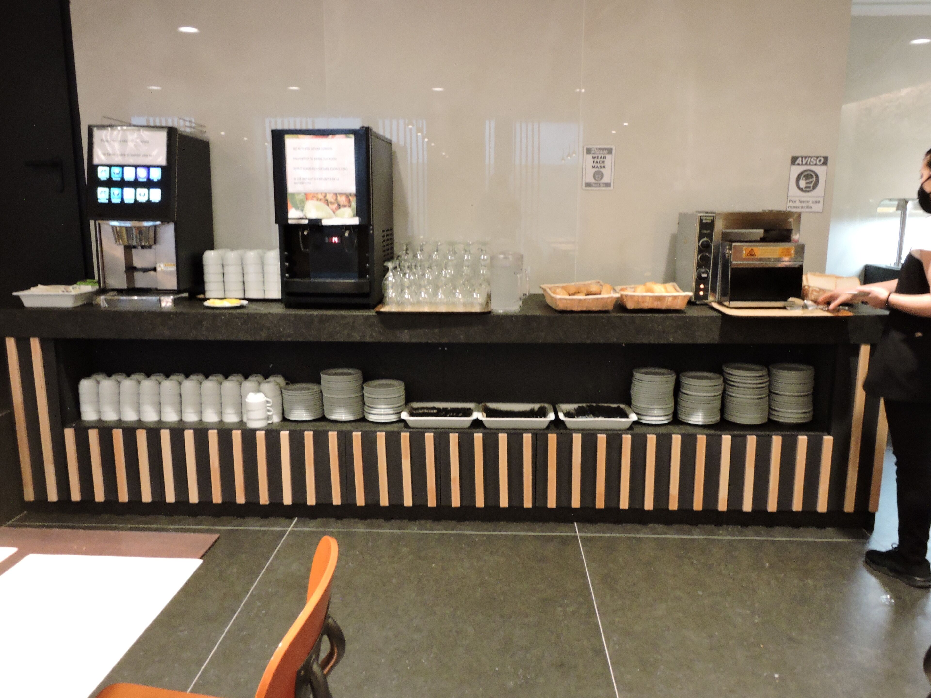 Un espace de libre-service proposant des boissons, avec une machine à café, un menu numérique et un présentoir pour les aliments.