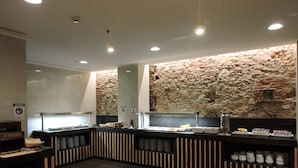 Un restaurant modern amb un mur de pedra de fons, decoració negra i de fusta, i un mostrador tipus bufet.