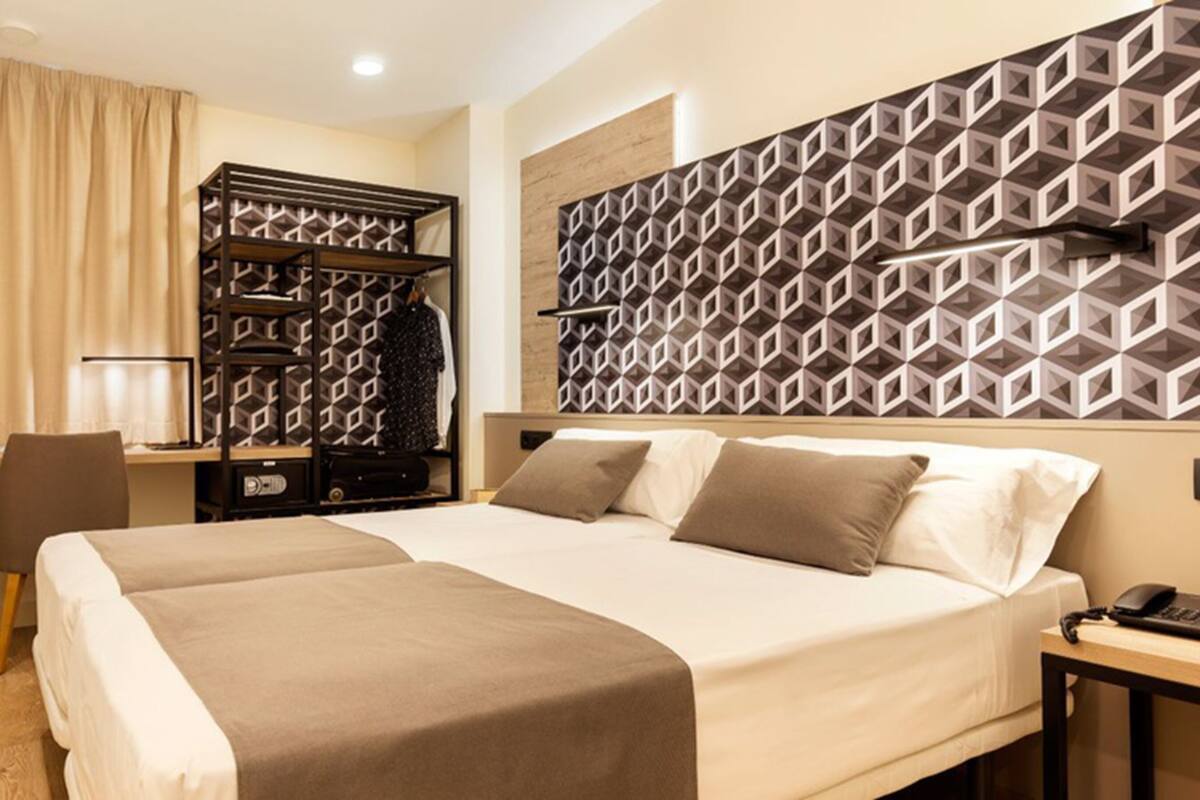 A hotel room with a large bed, a desk, a wardrobe, and a geometric-patterned headboard.