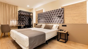 Habitació d'hotel moderna amb un llit gran, un armari, un escriptori i una obra d'art geomètrica penjada a la paret.