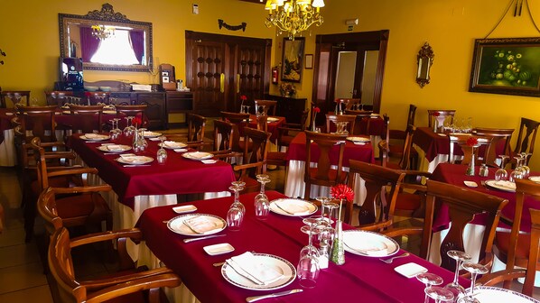 A dining area with tables set for multiple guests, featuring red tablecloths, white plates, and clear glassware.