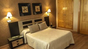A neatly arranged bedroom with a bed, nightstands, wall-mounted lamps, and a wardrobe. - Salvador Hotel (Bailen)
