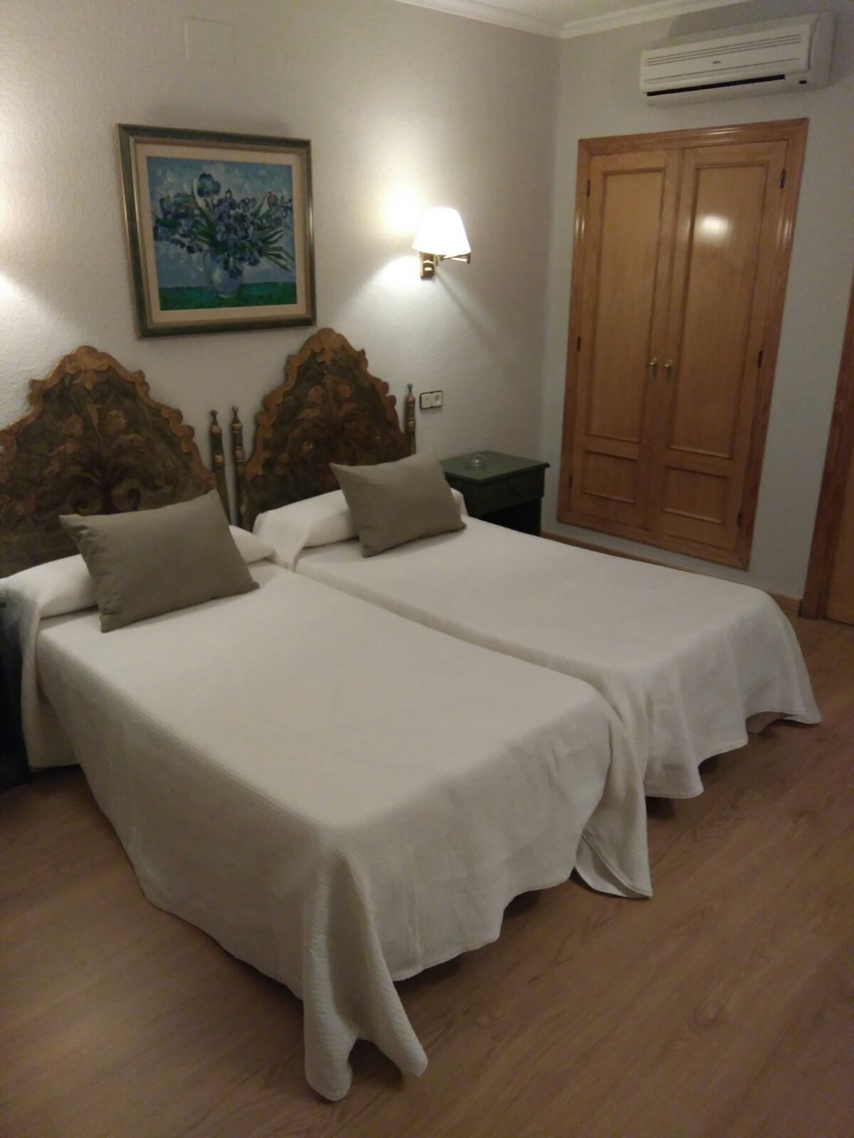 Habitación con dos camas, una mesita de noche, una lámpara de pared, un armario y un aire acondicionado.
