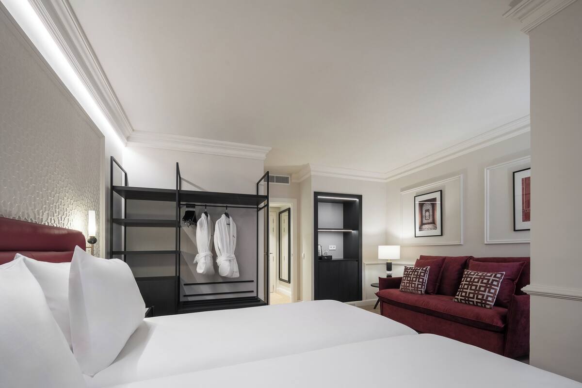 A hotel room with a large bed, a red sofa, a wardrobe, and a mirror.