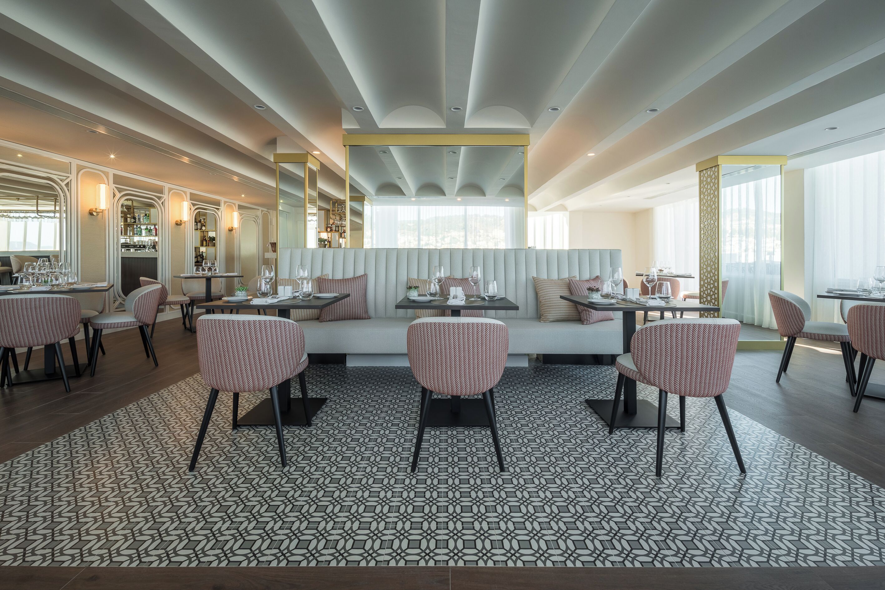 A modern restaurant with a patterned floor, cushioned seating, and a bar area.