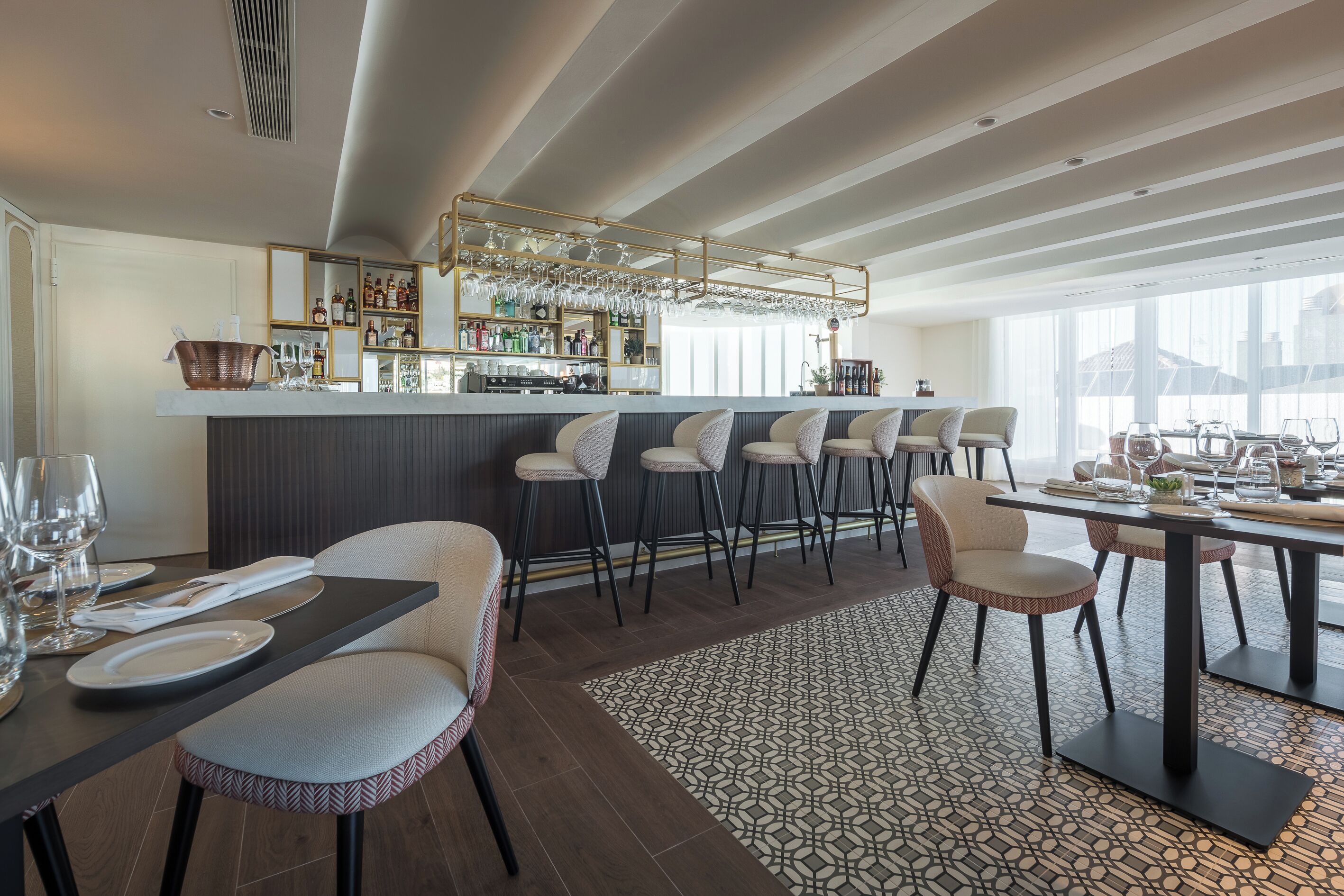 A modern bar area with a bar counter, stools, and a variety of bottles and glasses.