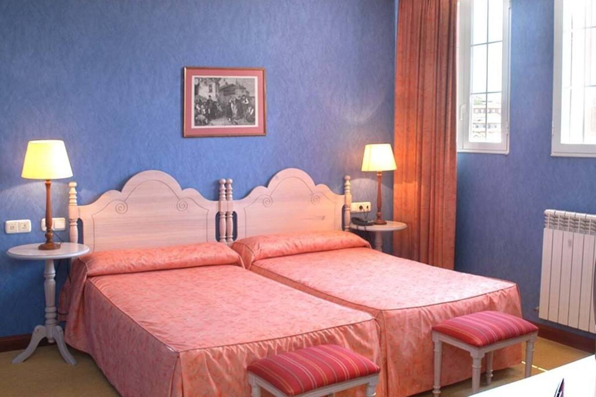 A bedroom with two beds, each with a matching headboard and footboard, flanked by bedside tables with lamps. A framed picture hangs on the wall above the beds.