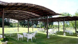 Un espacio al aire libre con sillas y mesas blancas bajo una estructura de techo de paja.