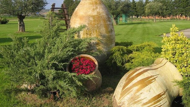 Un jardín con esculturas de piedra, una cerca de madera y diversas arbustos y flores.