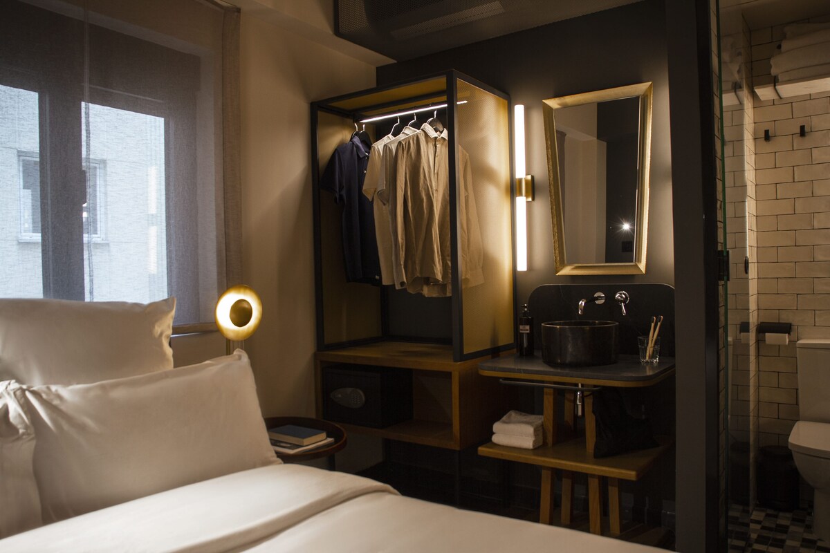 Een hotelkamer met een bed, nachtkastje, spiegel, kast, wastafel en toilet.