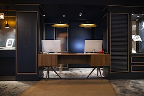 A modern office space with two desks, each with a computer and a lamp. There is a large mirror above the desks, and the room has a dark color scheme with gold trim. - Letoh Letoh Gran Vía (Madrid)