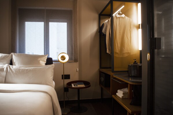 Hotellihuone, jossa on sänky, yöpöytä, lamppu, peili ja ikkuna, jossa on verhot.