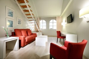 Una sala de estar moderna con un sofá rojo, una mesa de centro blanca y sillas rojas. Se observa una escalera con barandillas de madera, un televisor montado en la pared y cuadros enmarcados.