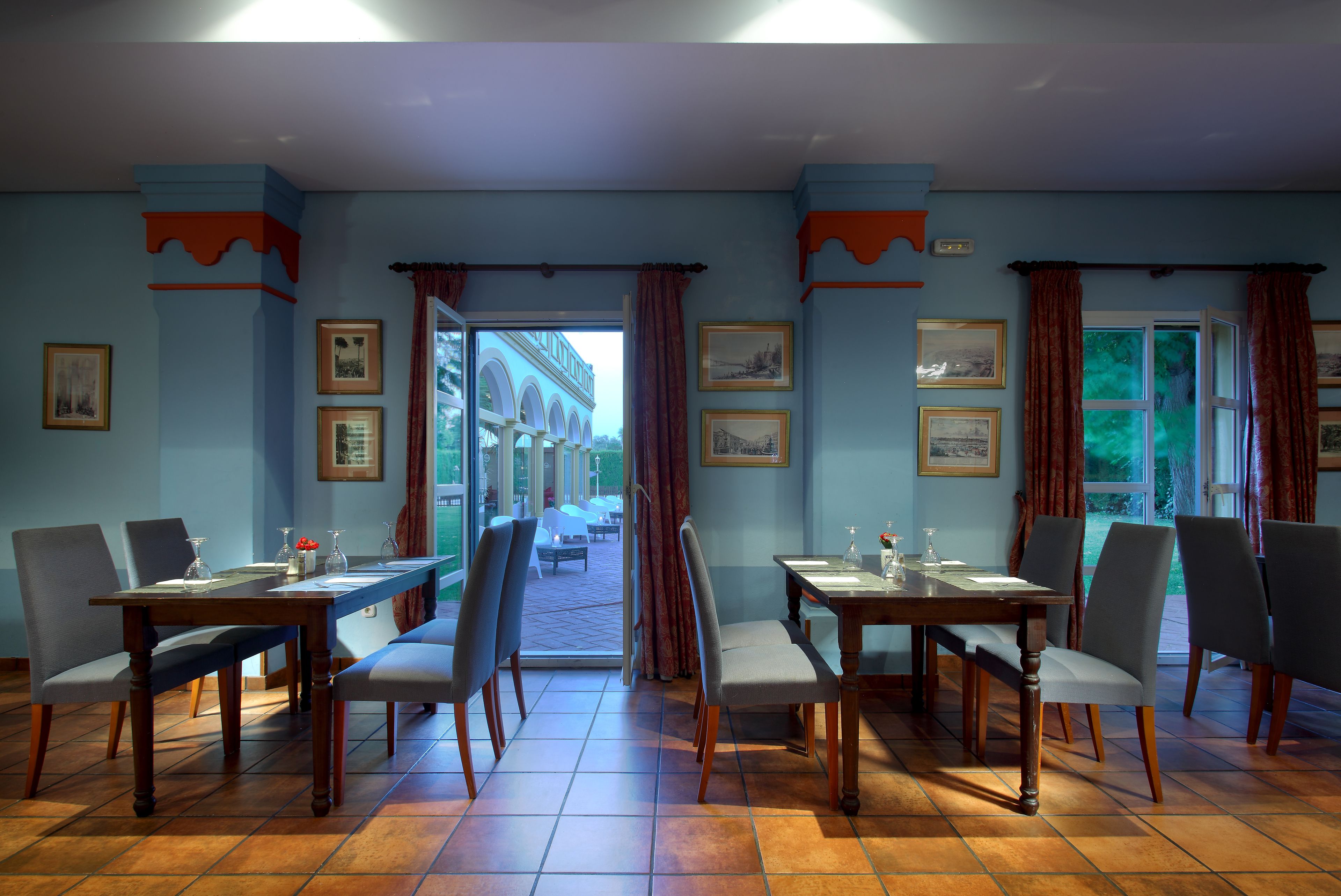Un comedor con una mesa larga y sillas, cuadros en las paredes y vistas a través de la puerta abierta.